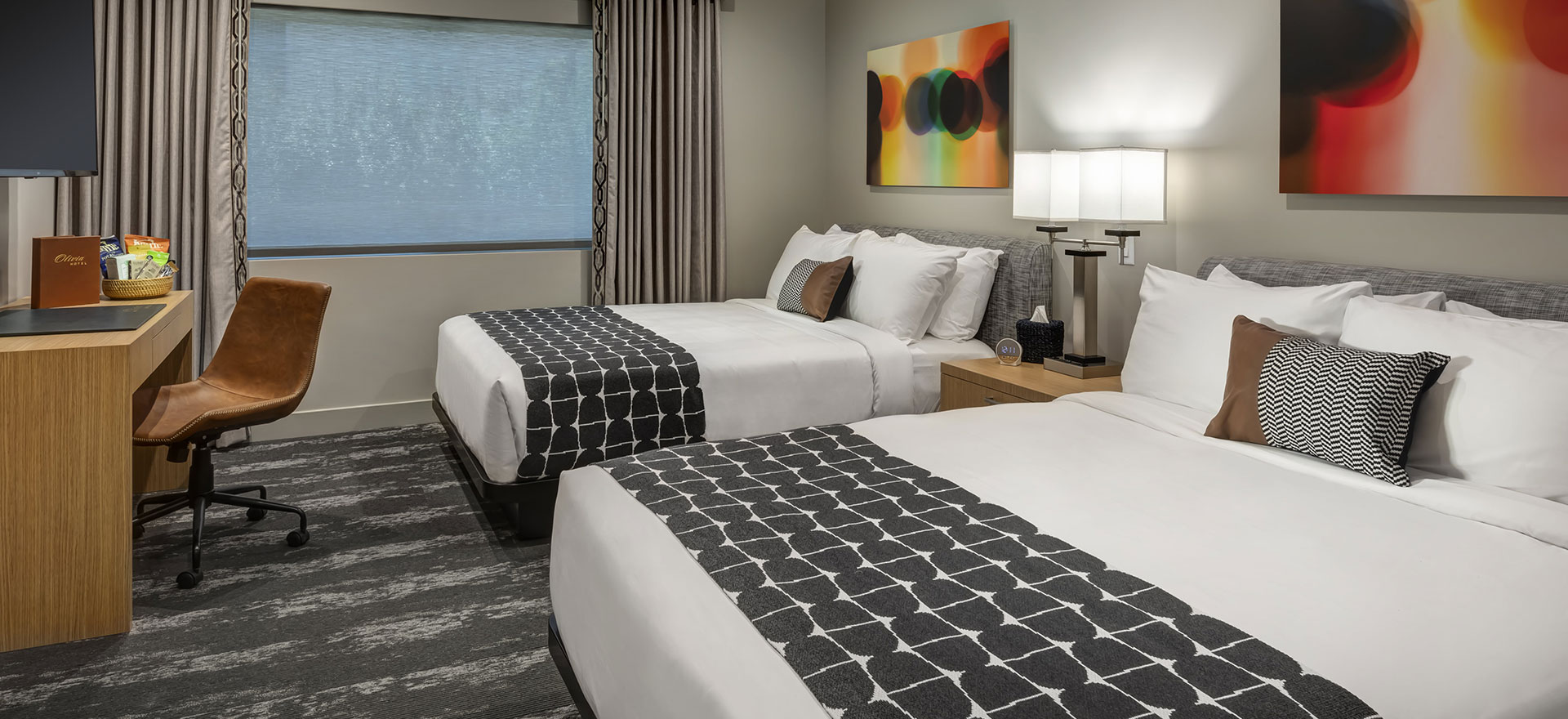 A hotel room with two beds, a window, and artwork on the wall.