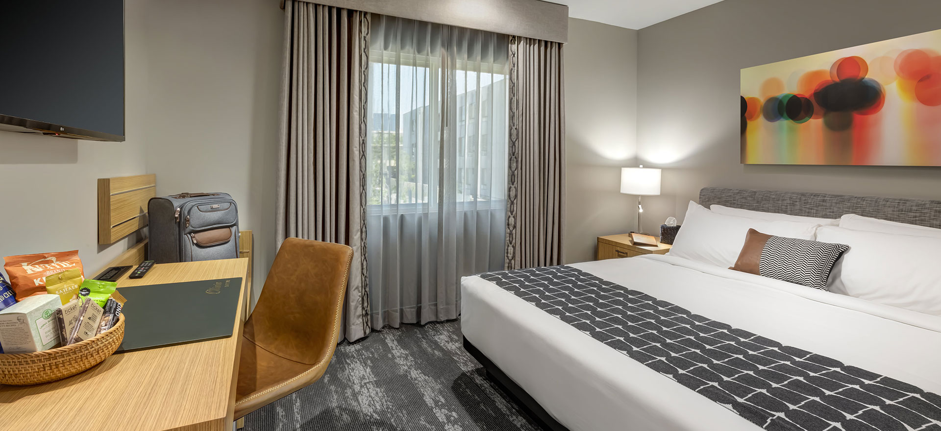 A hotel room with a bed, desk, chair, and window.
